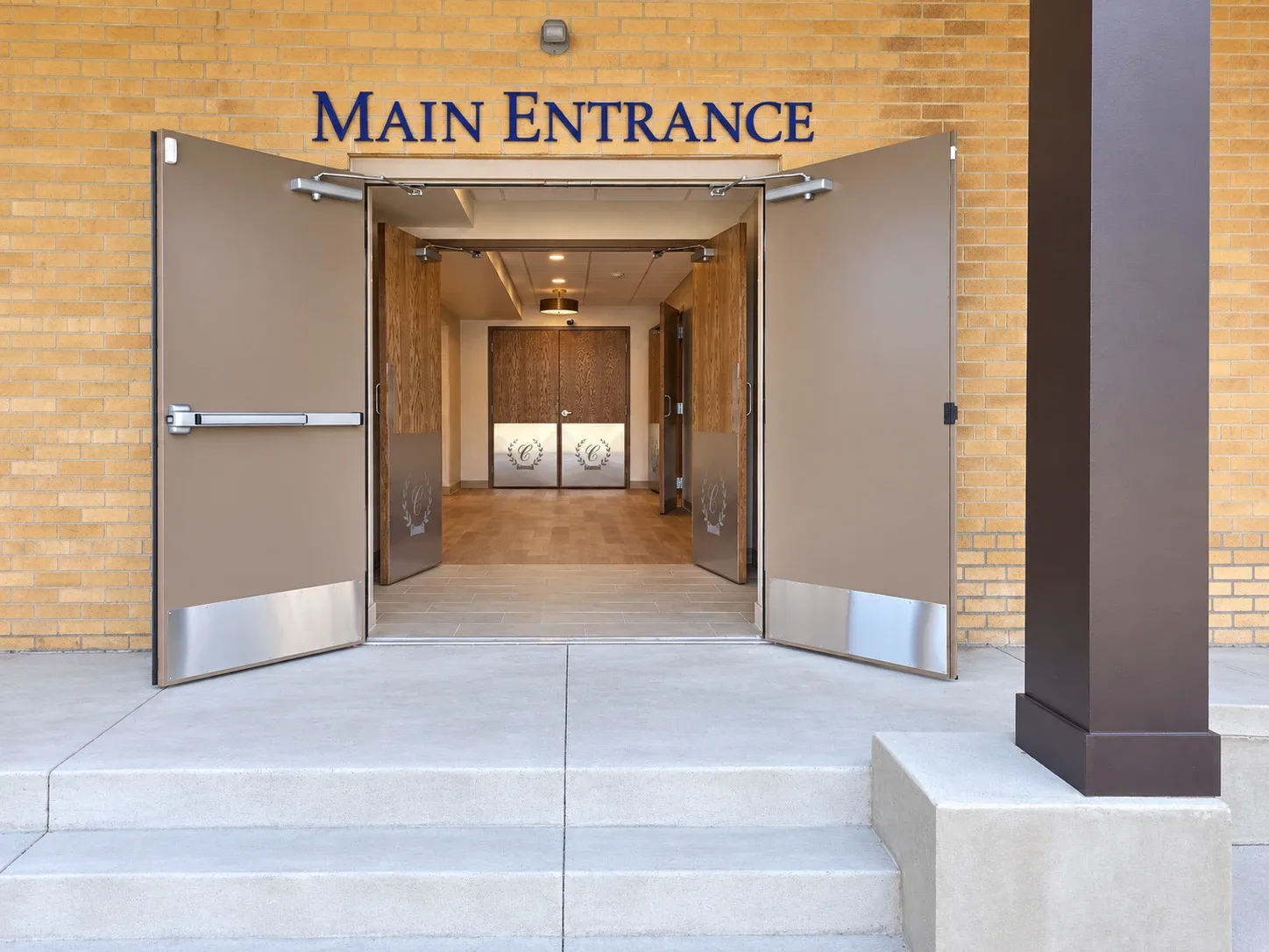 The main entrance of The Maria on the west side of the building, buff brick with MAIN ENTRANCE lettered above the open doors.