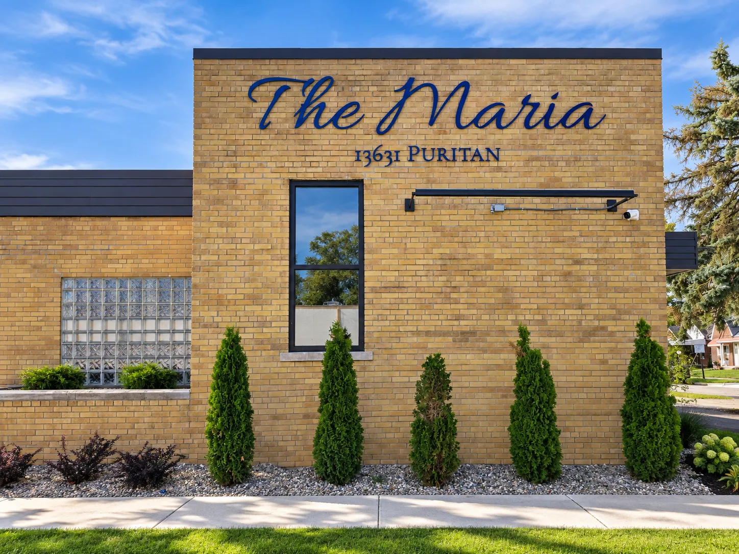 The north wall of The Maria, with the script wordmark and 13631 Puritan lettered in navy on the buff brick.